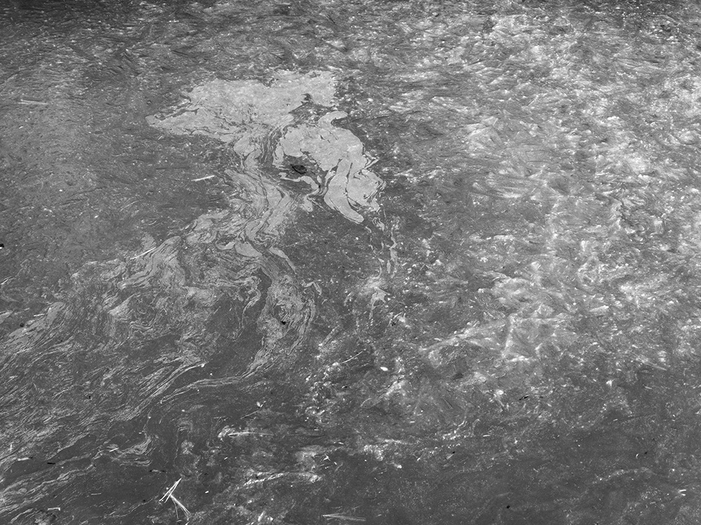 Black and White Photo of Abstract Patterns on Open River Ice.